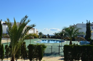 Una piscina rodeada de palmeras y una valla, con edificios al fondo.