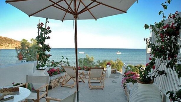 Zona esterna con posti a sedere e vista sul mare, con tavolo, sedie e un ombrellone grande.