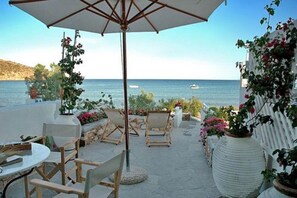 An outdoor seating area with a view of the sea, featuring a table, chairs, and a large umbrella.