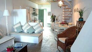 Un'accogliente zona giorno con un divano, un tavolo da pranzo e poltrone in vimini. Una scala con ringhiera in legno conduce a un'altra stanza.