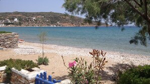 Una spiaggia costiera con un muro di pietra, una recinzione blu e vista sul mare e edifici in lontananza.
