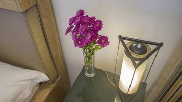 Ett litet bord med en vas med lila blommor och en vägglampa.