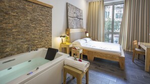 A modern hotel room with a large bathtub, a wooden bed, a small wooden table, and a view of the city through large windows. - Aquarooms (Palermo)