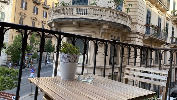 A wooden table with a potted plant and a glass bowl on a balcony with ornate black railings. - Aquarooms (Palermo)
