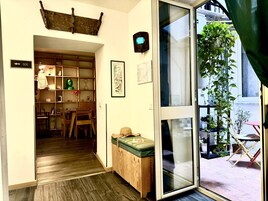 Una habitación con piso de madera, una puerta corrediza de vidrio que da a un balcón con plantas en macetas, un mueble de madera pequeño y un cuadro en la pared.