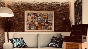 A cozy living room with a grey sofa, two patterned pillows, a wooden side table, a framed abstract painting, and a plant with green leaves. - Aquarooms (Palermo)