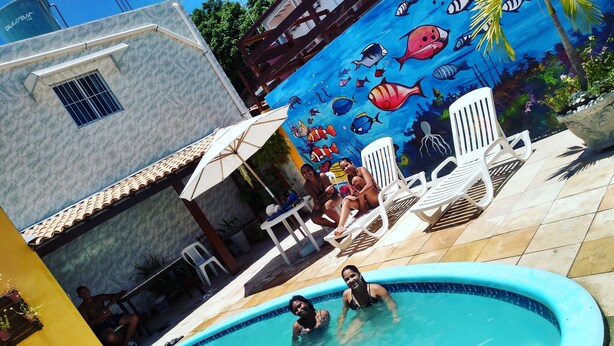 A swimming pool with a mural of fish, surrounded by white lounge chairs and a tiled patio area. - Suítes São Francisco (Ipojuca)