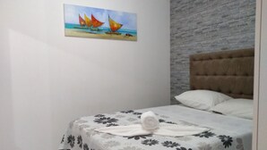 A bedroom with a bed, a painting of sailboats on the wall, and a tufted headboard. - Suítes São Francisco (Ipojuca)