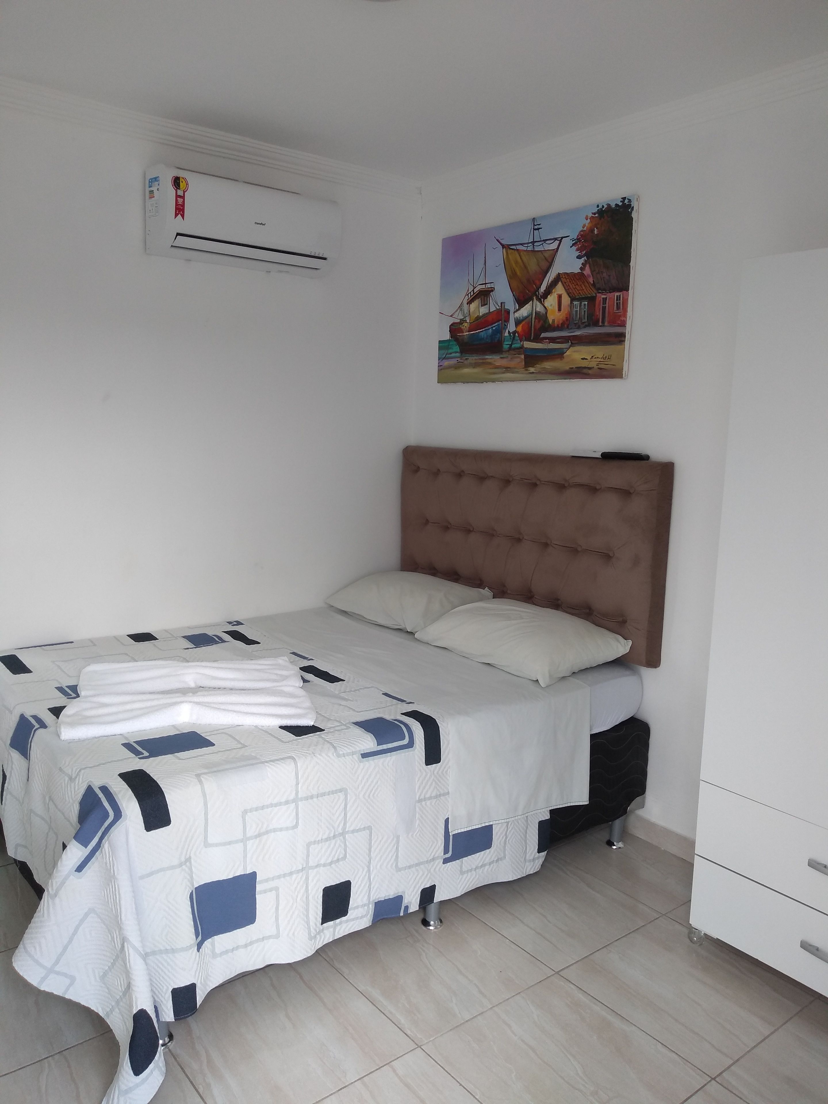 A bedroom with a bed, a headboard, a painting, an air conditioning unit, and a wardrobe.