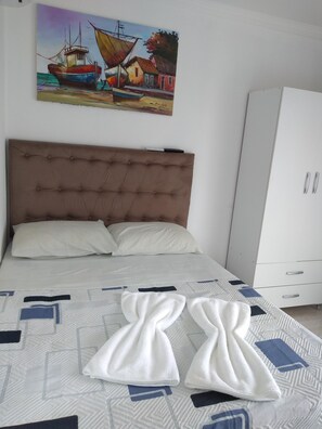 A bedroom with a large bed, a headboard, a wardrobe, and a painting on the wall. - Suítes São Francisco (Ipojuca)