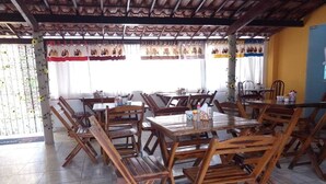 A restaurant with wooden tables and chairs, a tiled floor, and a covered outdoor area with a view of the street. - Suítes São Francisco (Ipojuca)