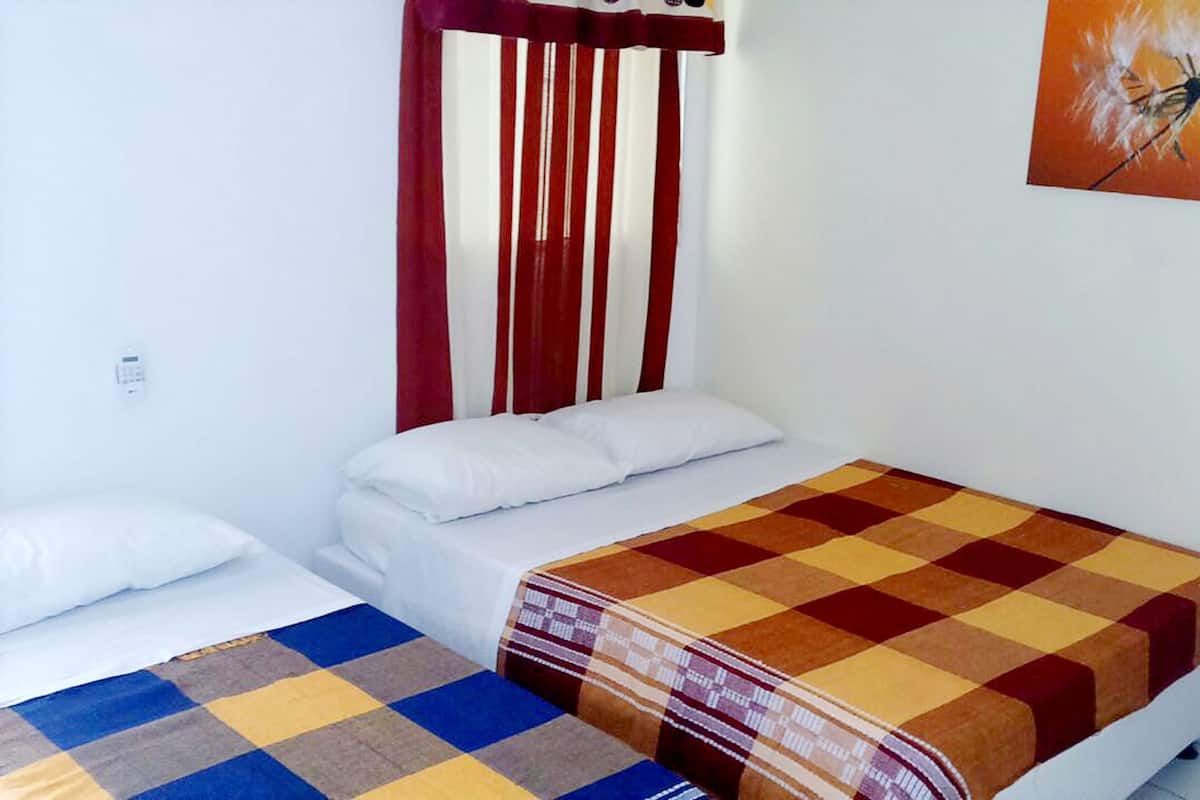 A small, clean room with two single beds, a wooden headboard, a white wall, and a painting of a dandelion.