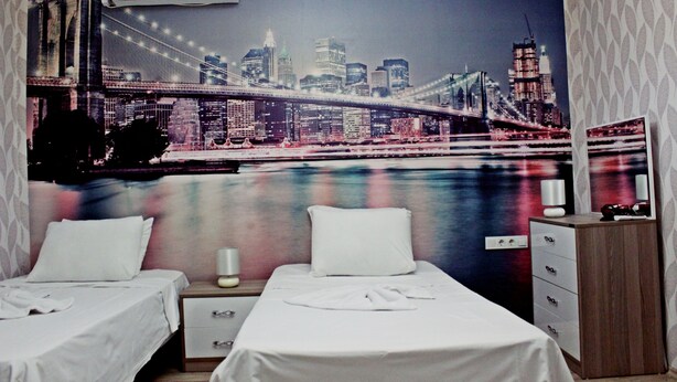 A hotel room with two beds, a nightstand, a dresser, and a large cityscape mural on the wall. - Tamara Suite Hotel (Istanbul)