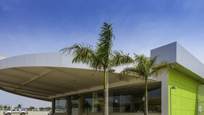 Un bâtiment moderne doté d’un toit incurvé, d’une façade verdoyante et d’un espace de stationnement où sont garées quelques voitures.