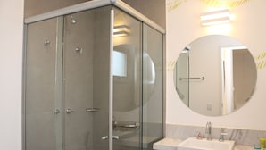 Un baño moderno con cabina de ducha de vidrio, un espejo redondo y un lavabo blanco con encimera de mármol.