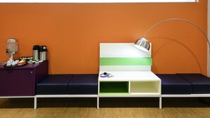 Un espace d’attente moderne comprenant un canapé, un coin café et un bureau avec une lampe.