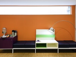 Uma área de espera moderna com um sofá, um espaço para café e uma mesa com abajur.