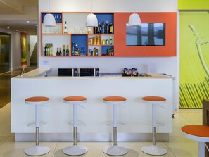 A bar area with stools, a TV, and shelves with bottles. - Ibis Styles Ponta Pora (Ponta Pora)