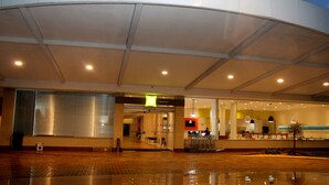 Entrada de un hotel moderno con fachada de vidrio, mostrador de recepción a la vista y un aviso de suelo mojado.