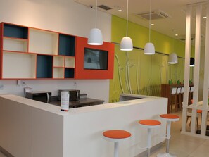 Uma área de recepção moderna com balcão, TV de tela plana e espaço de estar com bancos laranja.