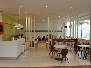 A modern restaurant interior with high ceilings, pendant lighting, and a mix of round and square tables.