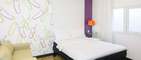 Hotellihuone, jossa on sänky, tuoli, pöytä, lamppu ja ikkuna.
