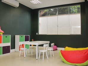 A room with a white table and chairs, a bean bag, a window with a view, and a cabinet with colorful storage compartments. - Ibis Styles Ponta Pora (Ponta Pora)