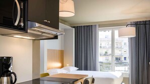 A compact hotel room with a kitchenette, a bed, a dining table, and a view of the city. - Aparthotel Adagio Access La Défense Puteaux (Puteaux)