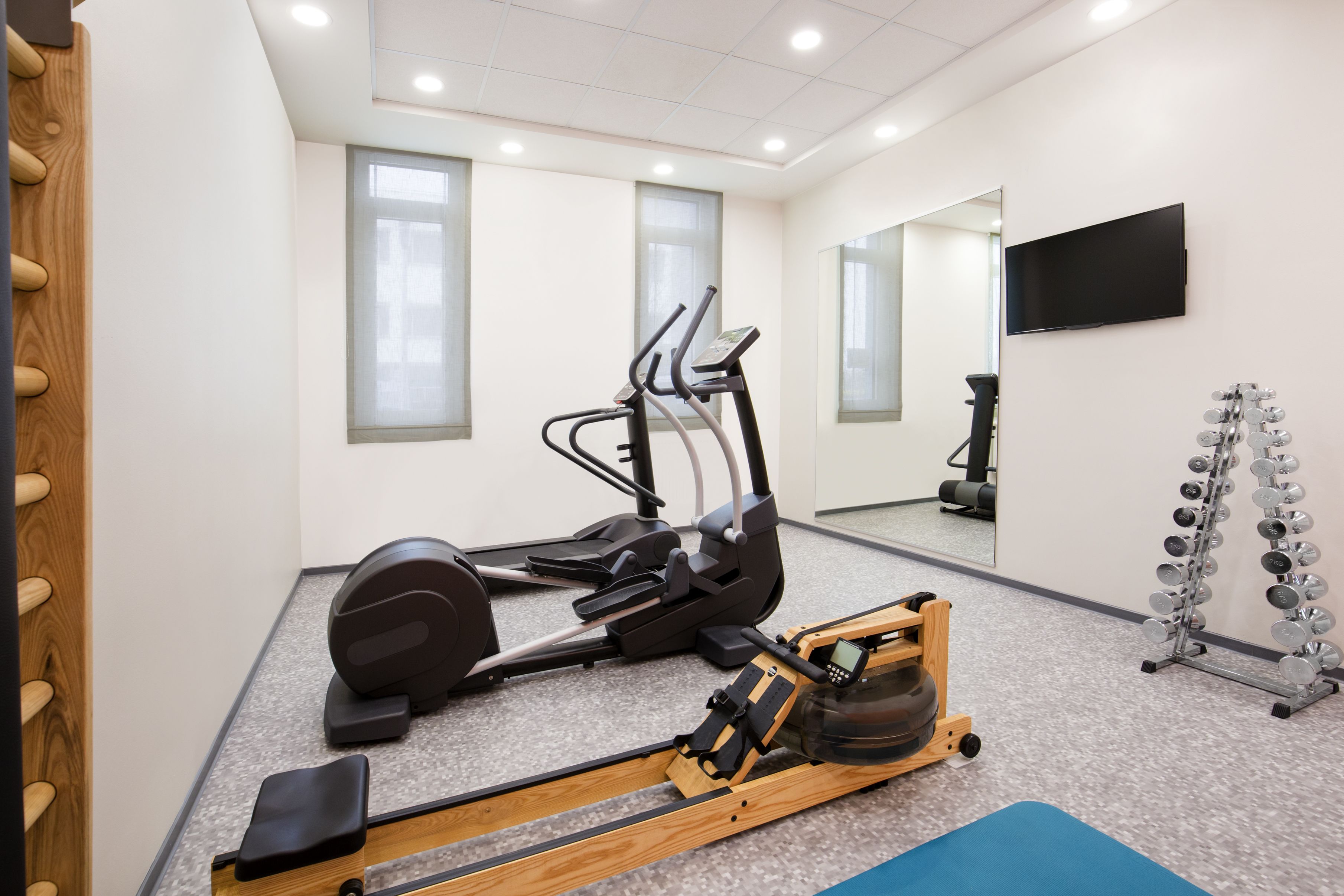 A gym with exercise equipment including a rowing machine, elliptical trainer, and a set of dumbbells.