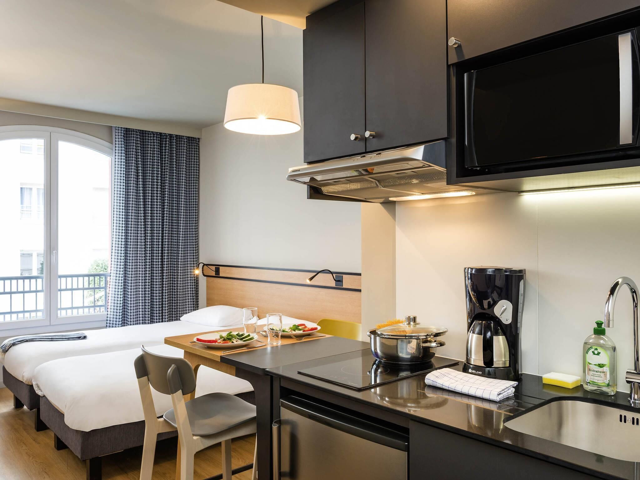 Een moderne hotelkamer met kitchenette, een bed, een eettafel met ontbijt en een groot raam.