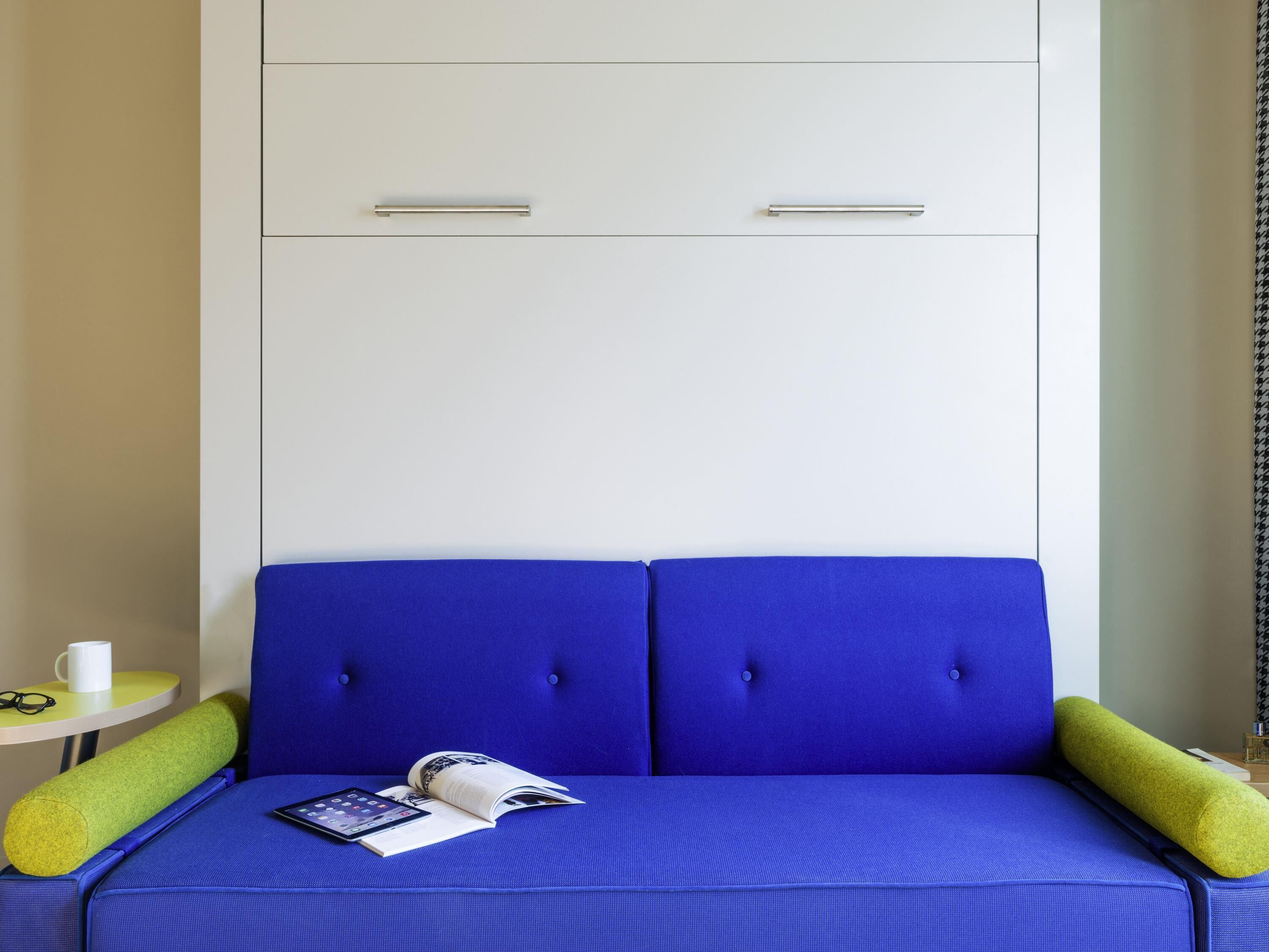 A room with a blue sofa, a small table with a cup and glasses, and a white wardrobe with two doors.