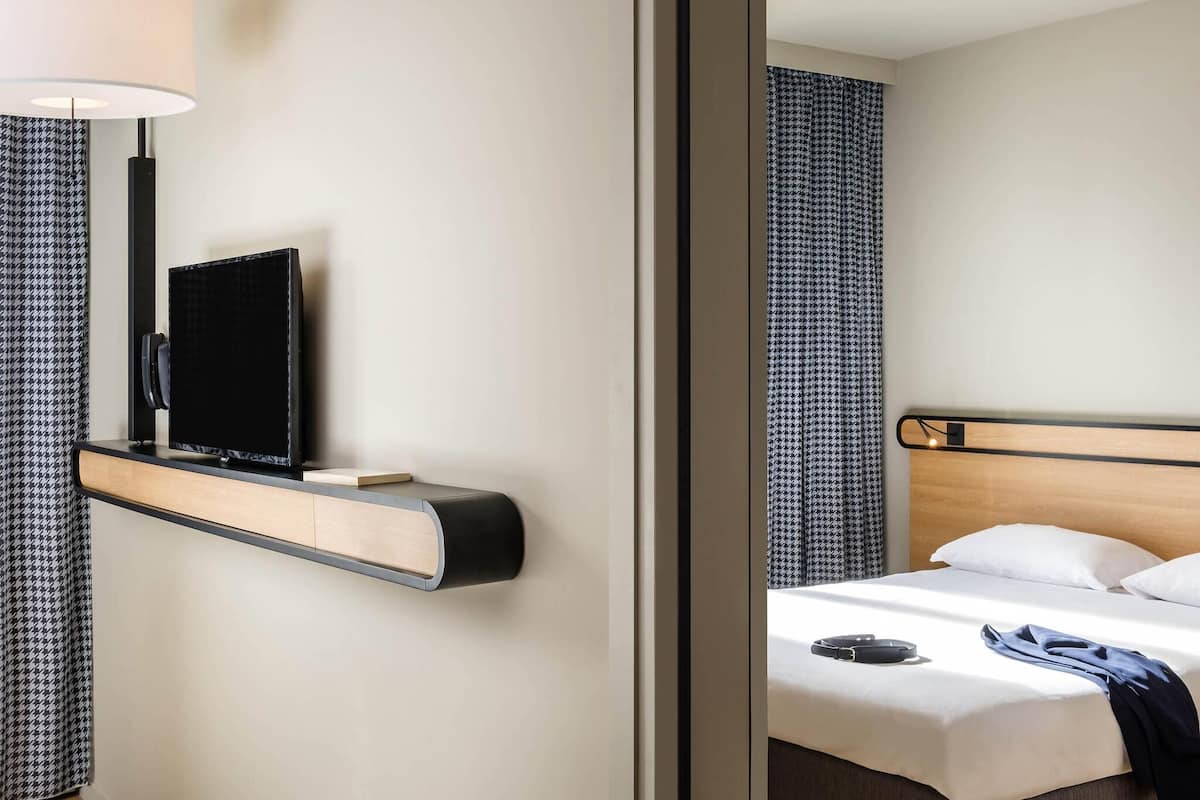 Ein Hotelzimmer mit einem Bett, einem Nachttisch mit Fernseher, einer Lampe und gemusterten Vorhängen.