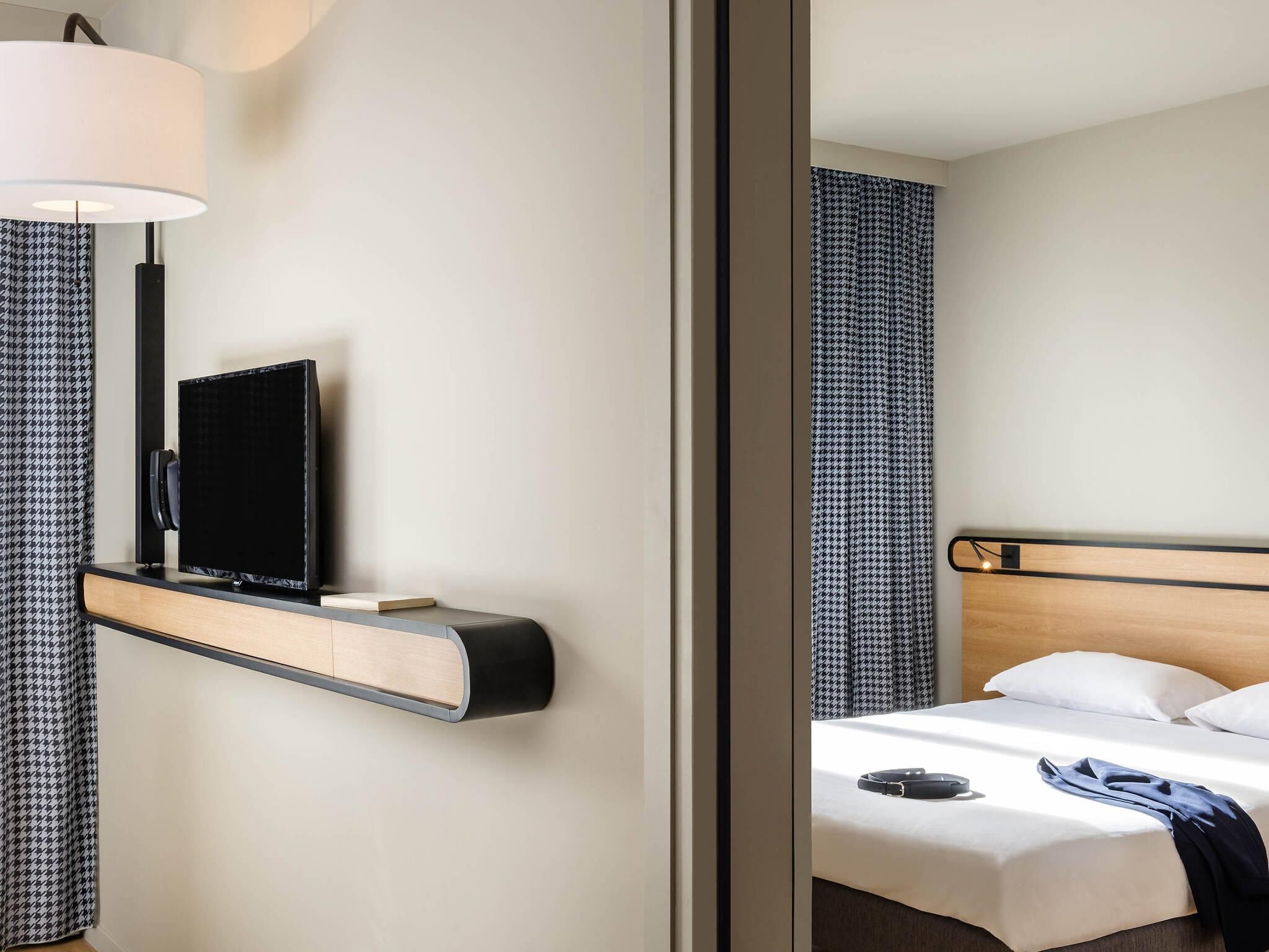Een hotelkamer met een bed, een nachtkastje met een televisie, een lamp en kamergordijnen met een patroon.