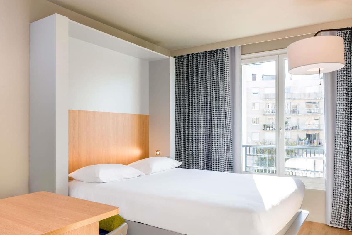 Ein modernes Hotelzimmer mit Bett, Schreibtisch und einem Fenster mit Vorhängen.
