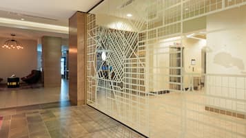 Un moderno vestíbulo de hotel con un separador de vidrio geométrico, una recepción y una zona de estar con sillones de cuero.