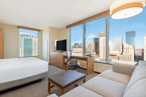 Une chambre d’hôtel équipée d’un lit, d’un bureau, d’une chaise, d’un canapé et d’une grande fenêtre donnant sur la ville.
