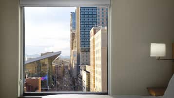 A hotel room with a large window offering a view of a cityscape, including tall buildings and a street.