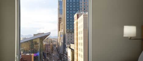 A hotel room with a large window offering a view of a cityscape, including tall buildings and a street.