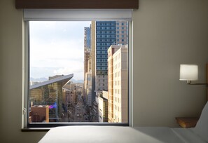 A hotel room with a large window offering a view of a cityscape, including tall buildings and a street. - Hyatt Place Denver Downtown (Denver)