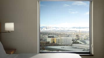 A hotel room with a large window offering a view of a cityscape and mountains.