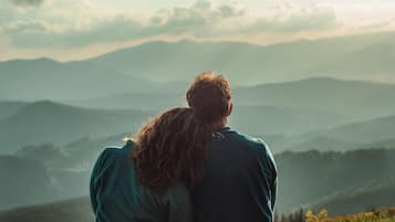 Una pareja sentada en una colina cubierta de hierba con vistas a una cadena montañosa.
