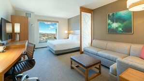 A hotel room with a bed, a sofa, a desk with a chair, a TV, and a large window with a city view. - Hyatt Place Denver Downtown (Denver)
