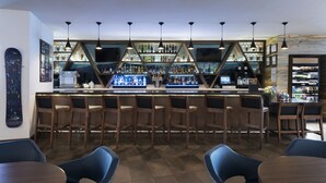 A bar area with wooden chairs, a counter with bottles, and pendant lights. - Hyatt Place Denver Downtown (Denver)