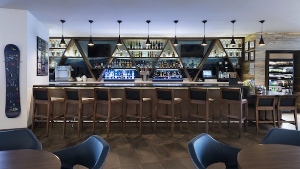 A bar area with wooden chairs, a counter with bottles, and pendant lights. - Hyatt Place Denver Downtown (Denver)