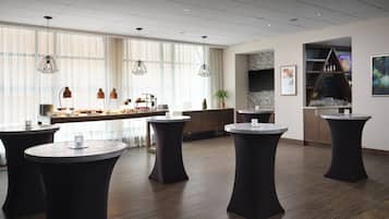 A modern lounge area with round tables, a bar, and large windows.