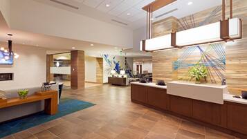 A modern reception area with a wooden reception desk, a seating area with a bench, and a wall with a geometric art piece.