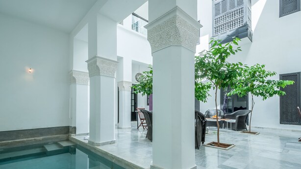 Un vaste espace intérieur doté d’une piscine, de colonnes blanches et d’un coin salon avec des chaises et une table.