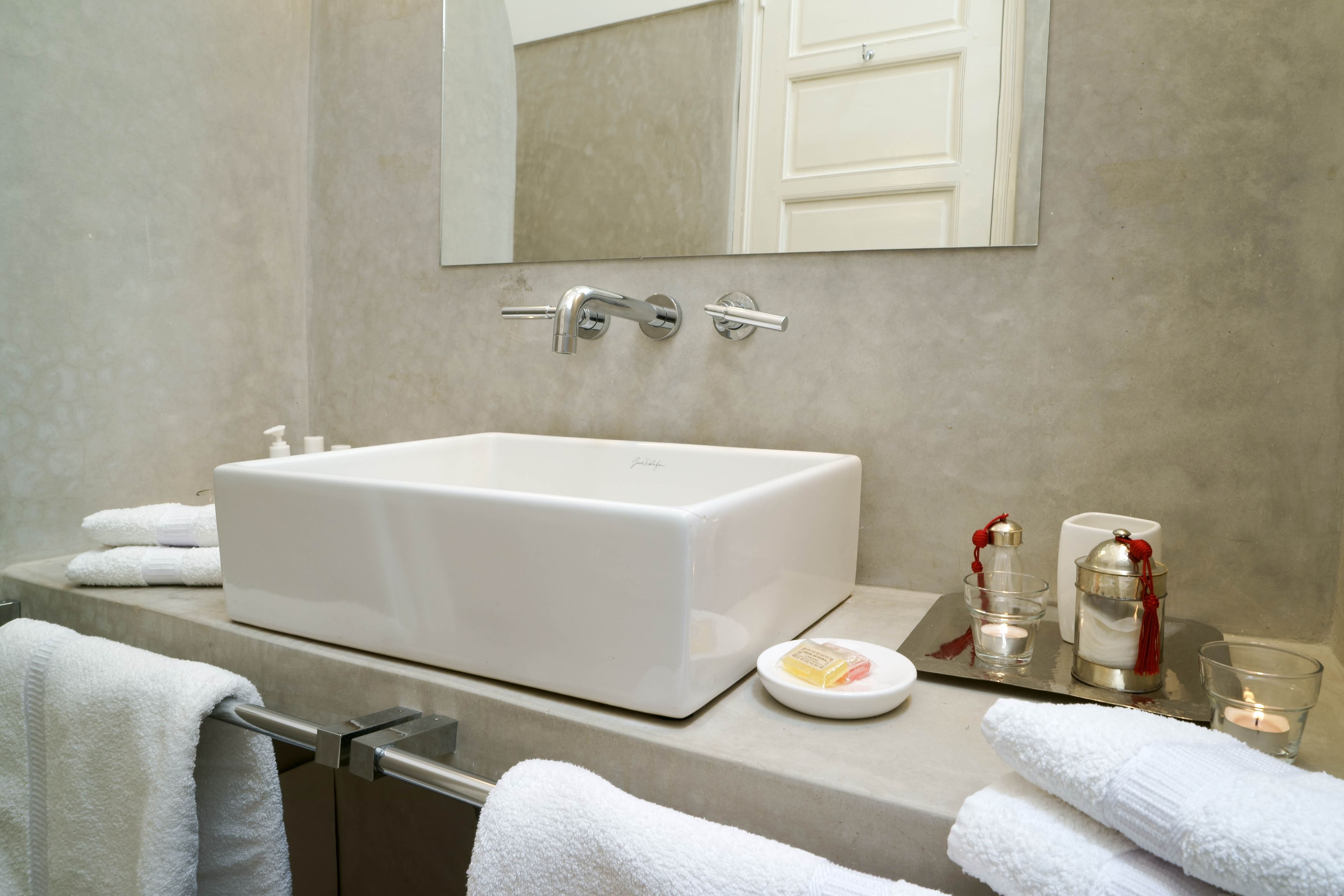 A bathroom with a large white sink, a mirror above it, and a towel rack with white towels.
