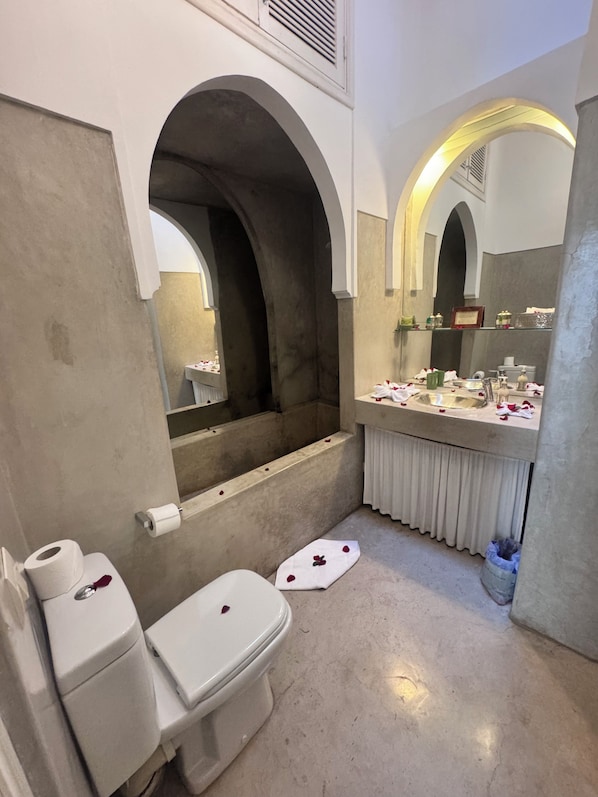 A bathroom with a bathtub, toilet, and sink, featuring arched alcoves and a mirror. - Riad Sapphire and Spa (Marrakech)
