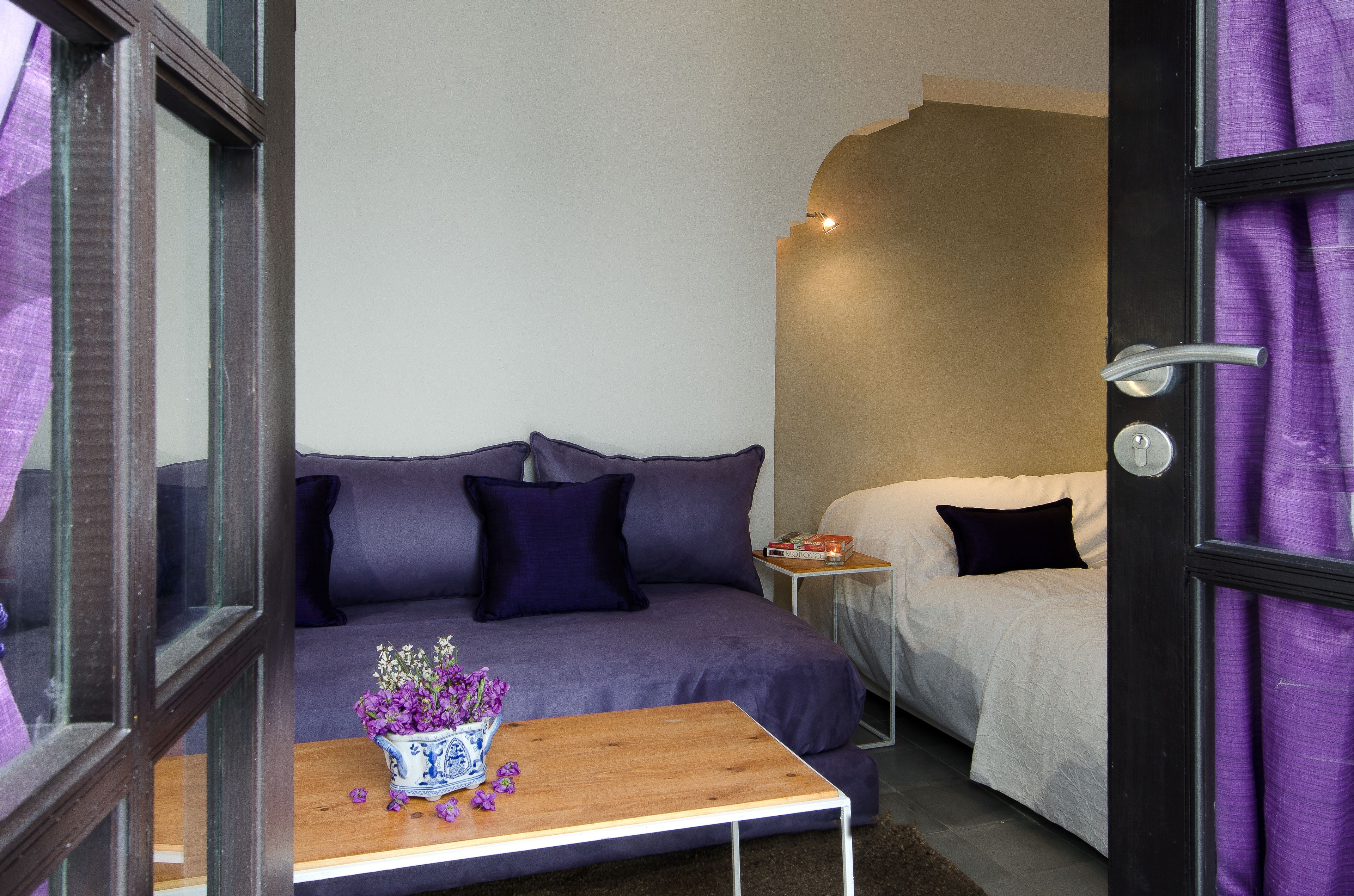 A room with a sofa, a small table with a vase, a bed, and a nightstand.